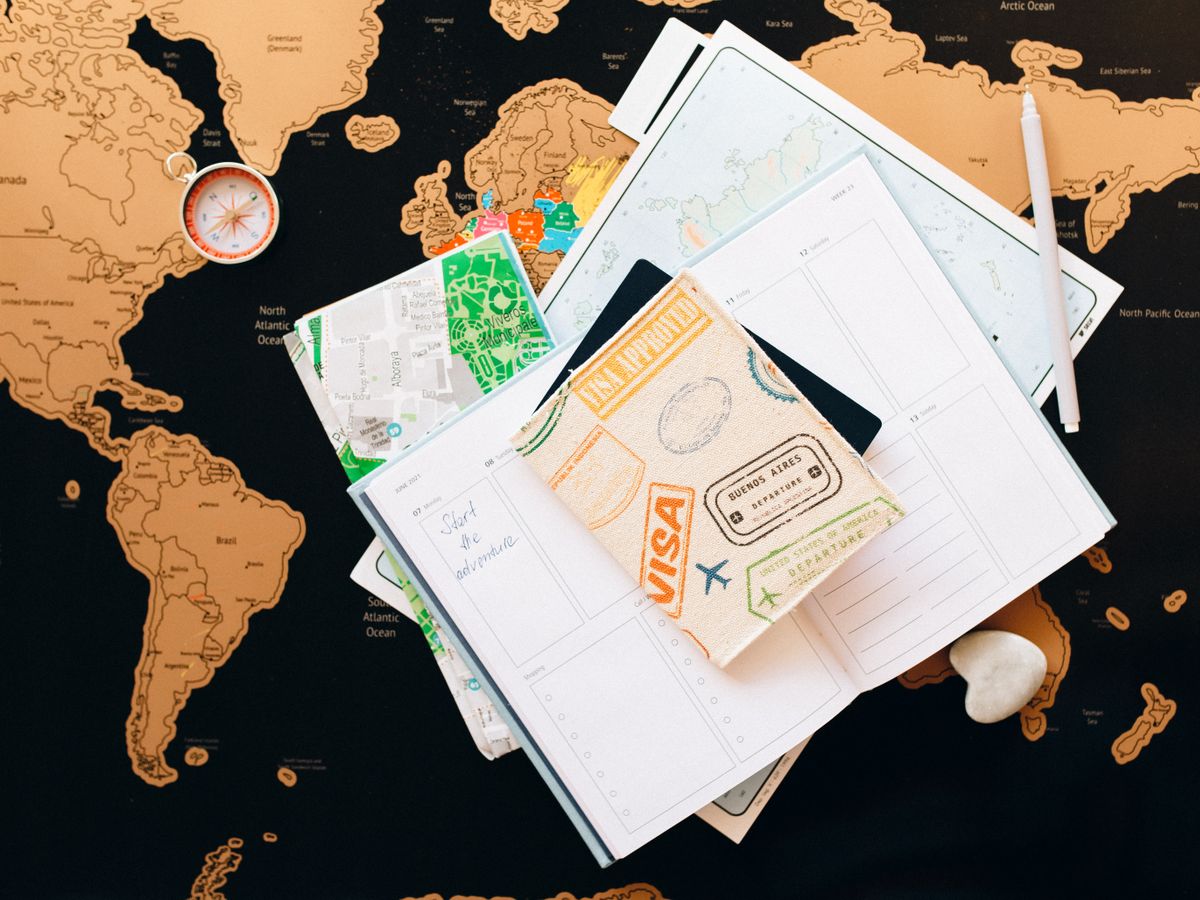 A passport with visa and departure stamps, a compass and a travel planner on a world map